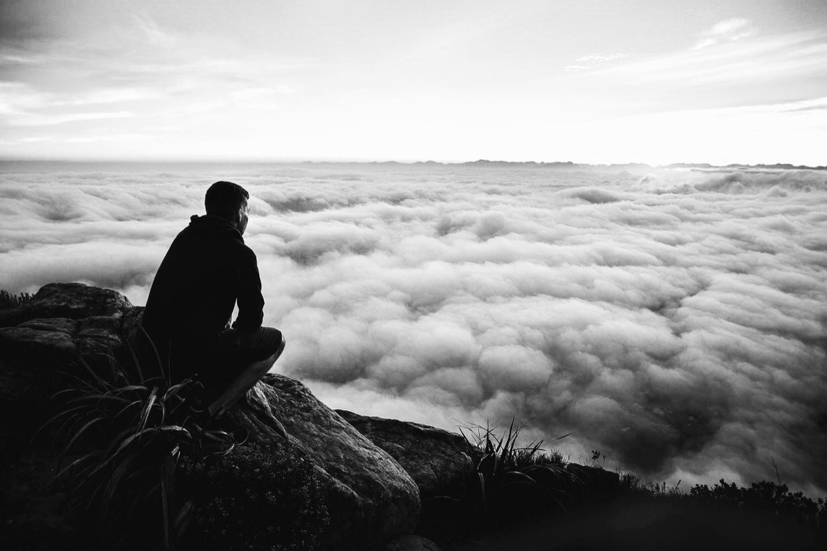 A person sitting on a mountain ridge above the clouds